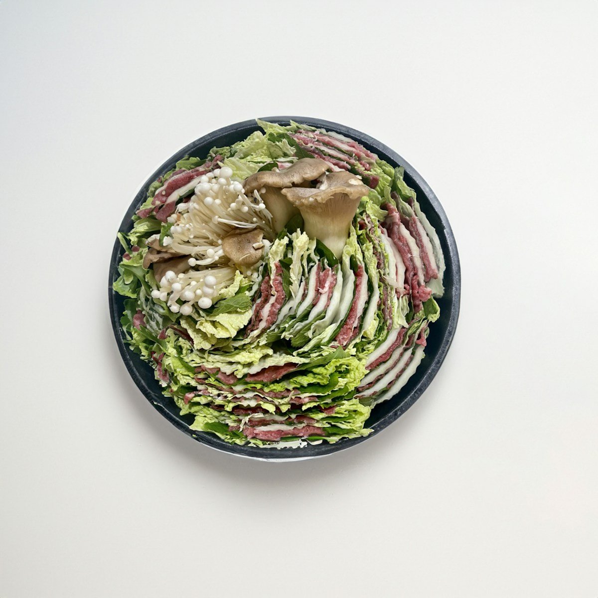 a bowl of lettuce and other vegetables on a white surface